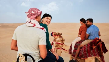 Travellers riding camels across the Abu Dhabi desert during a guided camel trekking tour
