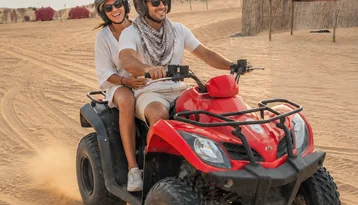 Couple riding a red quad bike on Abu Dhabi desert dunes during a sunset safari