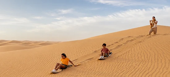 Children sandboarding on a family desert safari
