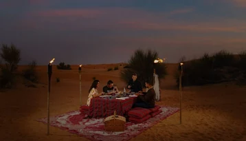 Guests enjoying a private desert dinner with torch lights and traditional floor seating in the Abu Dhabi dunes