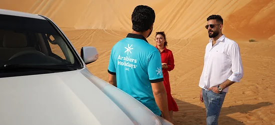 An Arabiers safari guide speaking with guests beside a 4x4 in the desert