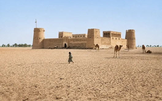 Historic Qasr Al Hosn fort in Abu Dhabi surrounded by desert landscape and camels