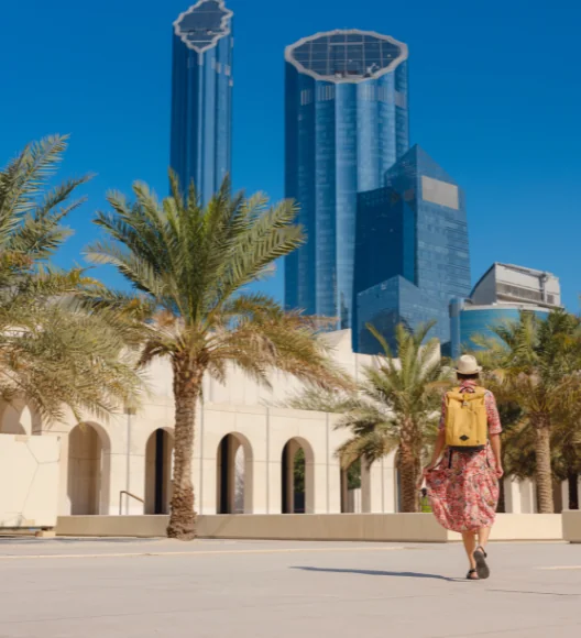 Tourist walking near palm trees with Abu Dhabi skyline in the background