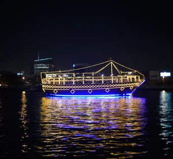 Illuminated Dubai dhow cruise boat sailing at night with reflections on the water, destination guide by Martin Muthugumi for Arabiers