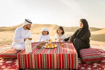 Family seated at a traditional majlis style table in the Abu Dhabi desert during a private dinner experience arranged by Mujeeb Rahman for Arabiers Holidays