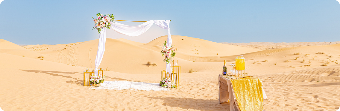 Luxury private dune wedding venue in Dubai with floral arch, lantern décor and champagne table set against golden desert dunes
