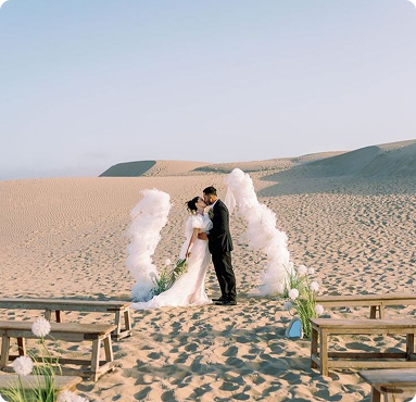 Minimalist desert wedding ceremony in Dubai with bride and groom under white arch on private sand dunes