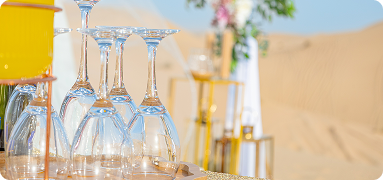 Luxury refreshment table setup at a desert wedding venue in Dubai with crystal glasses and golden décor on sand dunes
