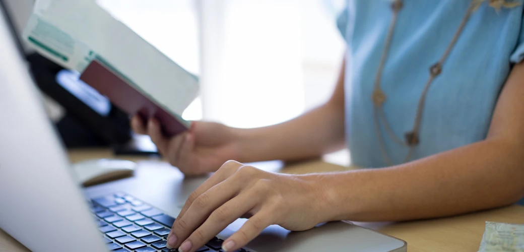 Traveller holding a passport while using a laptop for an online visa application