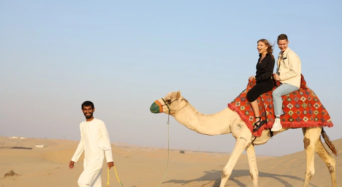 Guide leading a camel with guests across the Abu Dhabi desert dunes