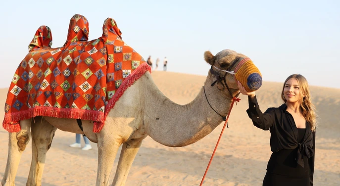Guest beside a camel with a colourful traditional saddle in the Abu Dhabi desert
