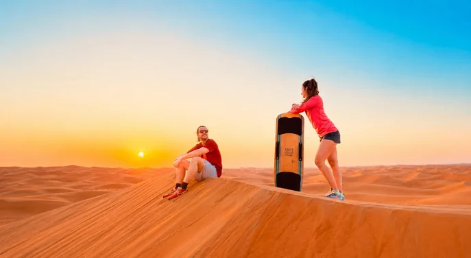 Guests with a sandboard on the Al Khatim dunes at sunset