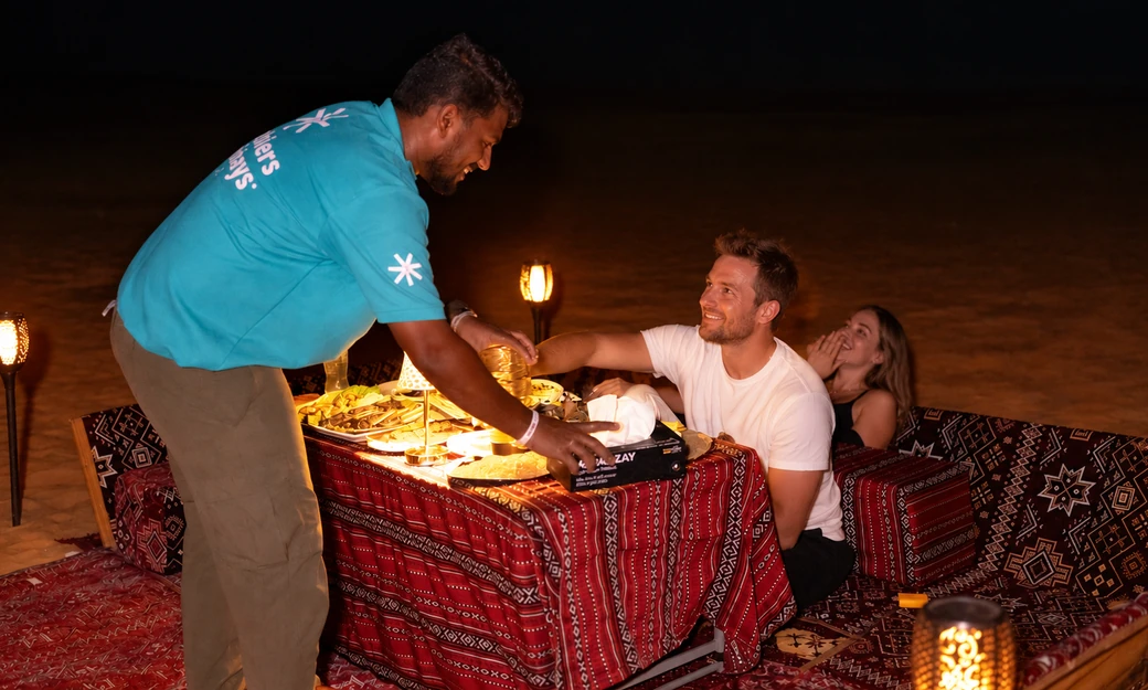 Arabiers team member serving guests at a private desert dinner setup in Al Quaa