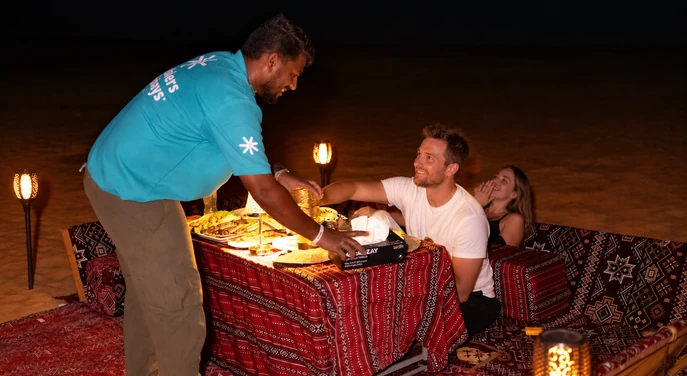 Arabiers team member serving guests at a private desert dinner setup in Al Quaa