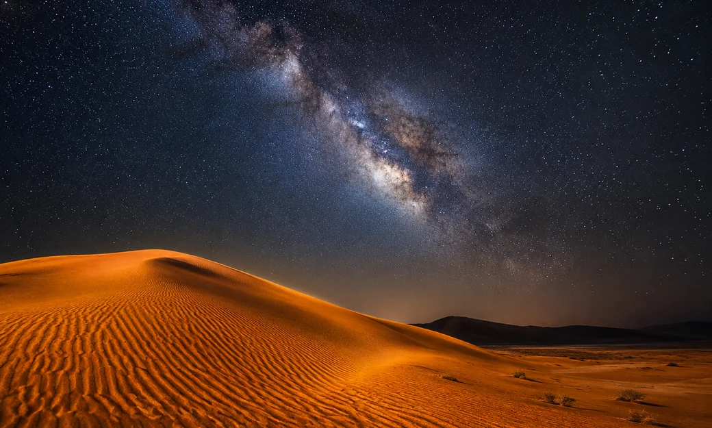 Milky Way stretching above illuminated dunes at Al Quaa desert