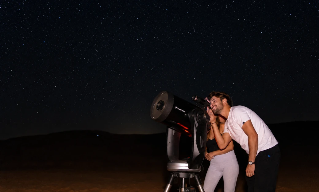 Couple using a telescope during a stargazing experience at Al Quaa desert