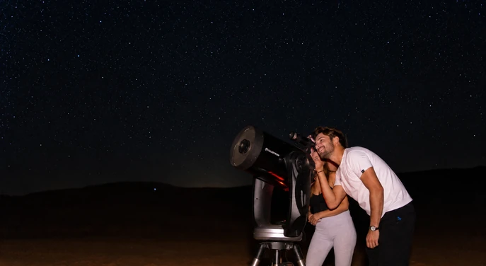 Couple using a telescope during a stargazing experience at Al Quaa desert