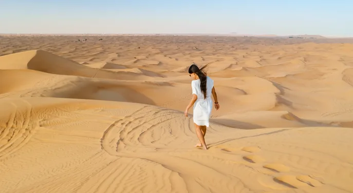 Traveller walking barefoot across the Abu Dhabi dunes in the morning