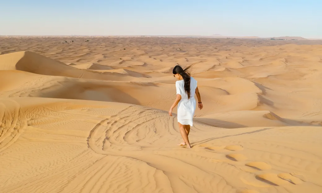 Traveller walking barefoot across the Abu Dhabi dunes in the morning