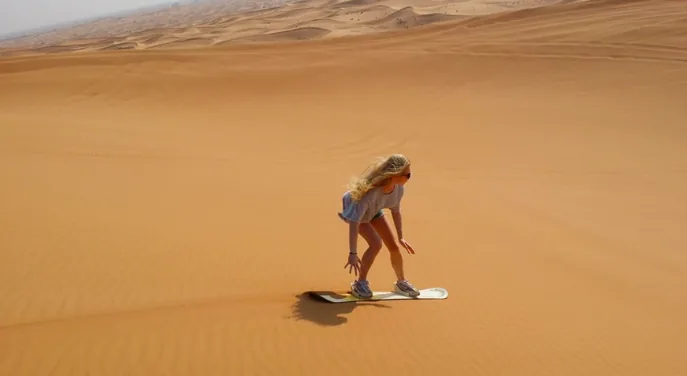 Traveller sandboarding during a morning Abu Dhabi desert experience