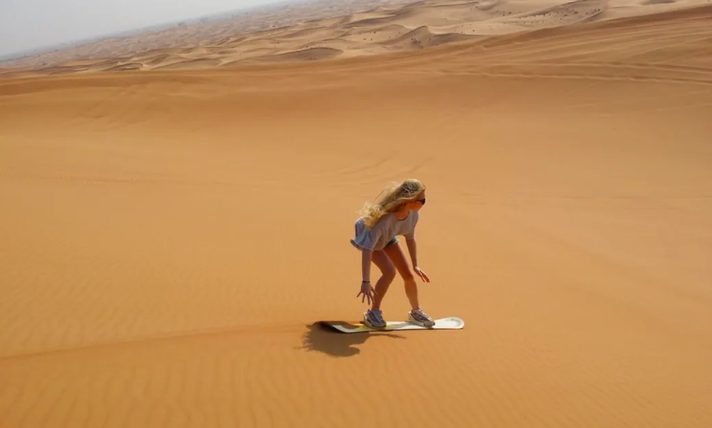 Traveller sandboarding during a morning Abu Dhabi desert experience
