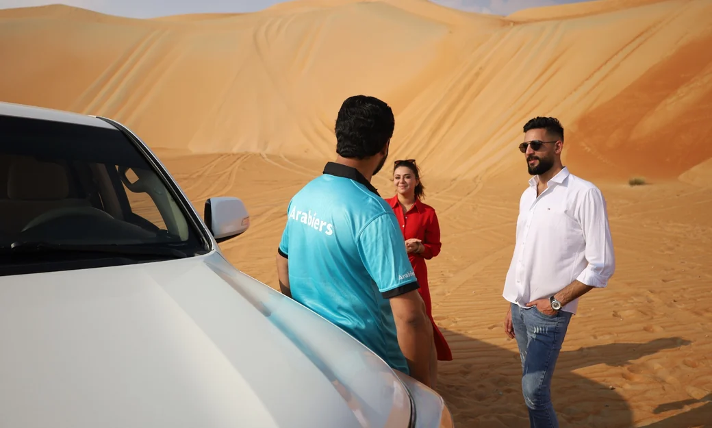 Arabiers desert guide speaking with a couple beside a Land Cruiser in Liwa