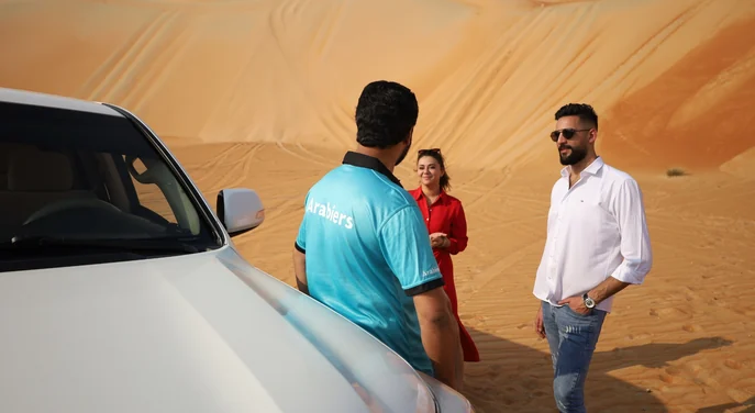 Arabiers desert guide speaking with a couple beside a Land Cruiser in Liwa