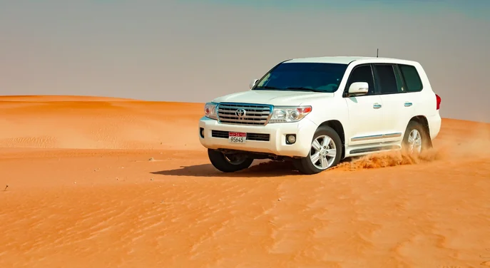 White Toyota Land Cruiser driving across the Liwa desert on a guided day tour