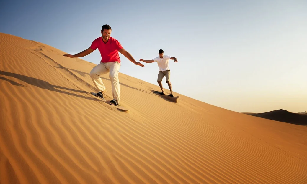 Two travellers sandboarding together on the golden dunes of Liwa