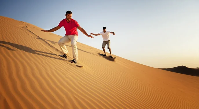 Two travellers sandboarding together on the golden dunes of Liwa