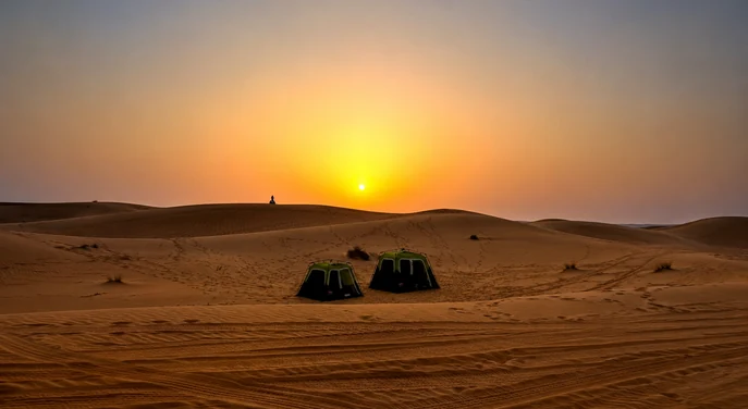 Two camping tents set among Liwa desert dunes during sunset