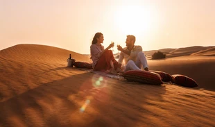 Couple toasting champagne on a private rug setup at sunset in the Liwa desert