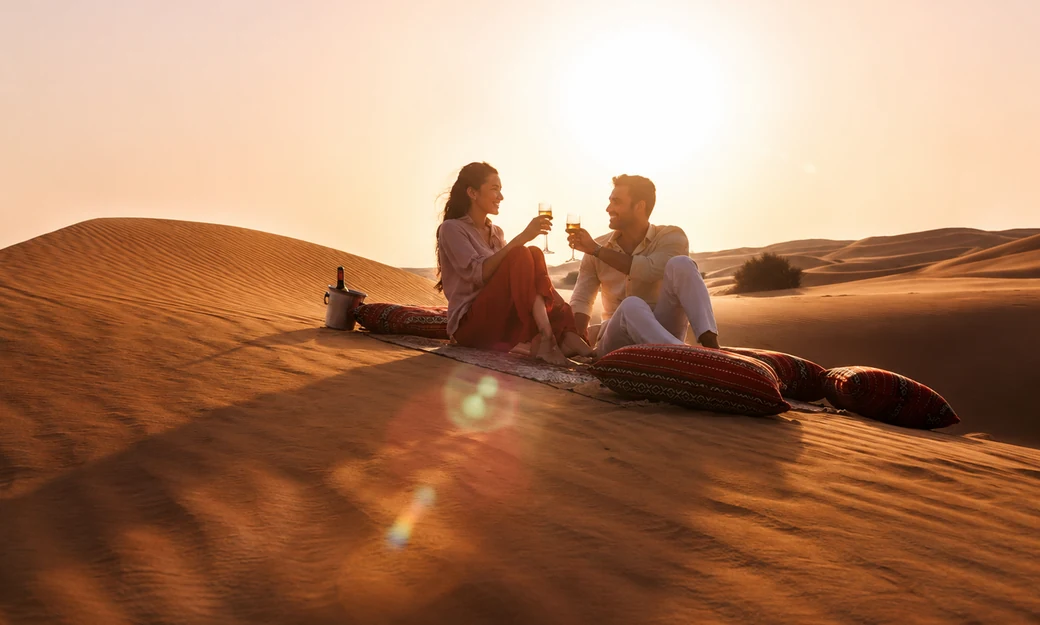 Couple toasting champagne together on a private rug setup at sunset in the Liwa desert