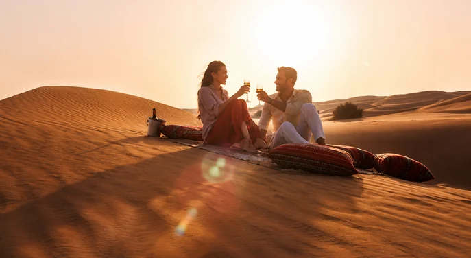 Couple toasting champagne together on a private rug setup at sunset in the Liwa desert