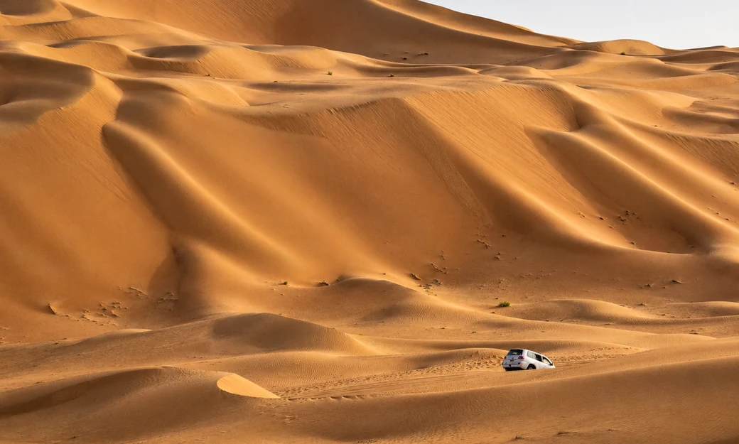 Sweeping Liwa dunes with a white four wheel drive crossing the desert below