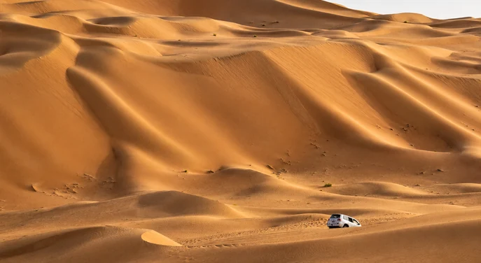 Sweeping Liwa dunes with a white four wheel drive crossing the desert below