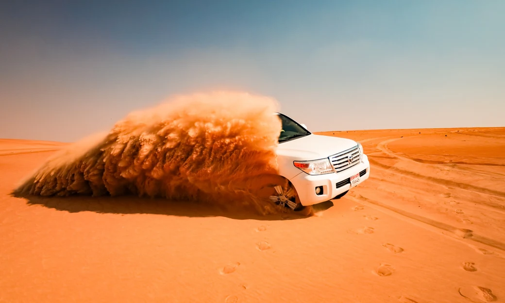 White Toyota Land Cruiser climbing a high orange dune in Liwa