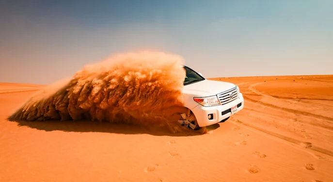 White Toyota Land Cruiser climbing a high orange dune in Liwa