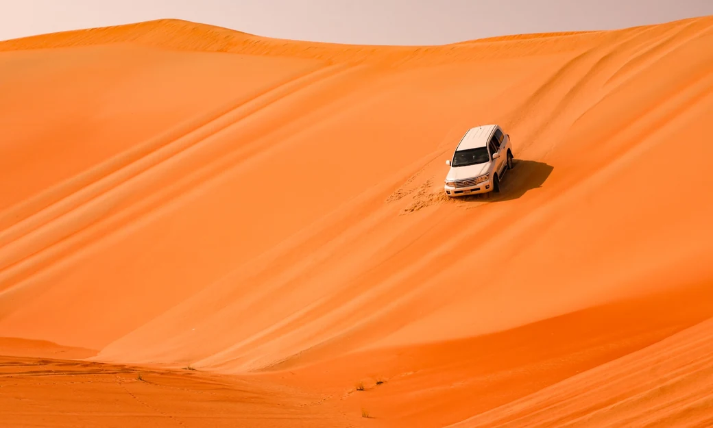 White Toyota Land Cruiser kicking up sand while crossing the Liwa desert
