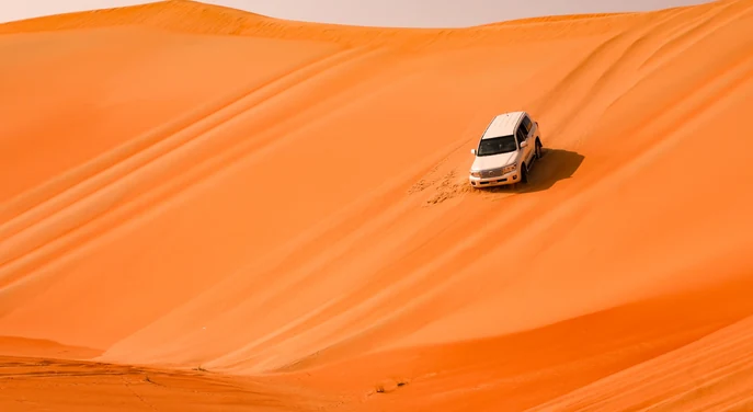 White Toyota Land Cruiser kicking up sand while crossing the Liwa desert