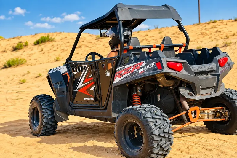 Polaris RZR 900 dune buggy with a helmeted driver on the Abu Dhabi dunes
