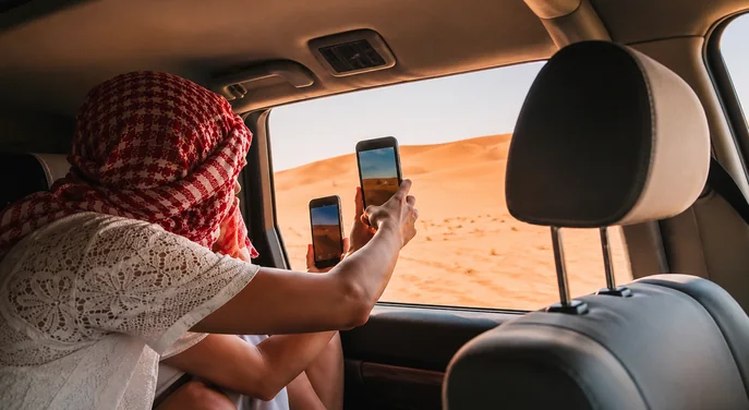 Handler leading a private camel procession across pale Abu Dhabi desert dunes