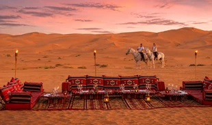 Private torch-lit BBQ dining setup at sunset in the Liwa dunes near Qasr Al Sarab