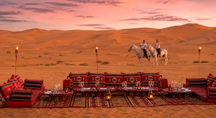 Private torch-lit BBQ dining setup at sunset in the Liwa dunes near Qasr Al Sarab