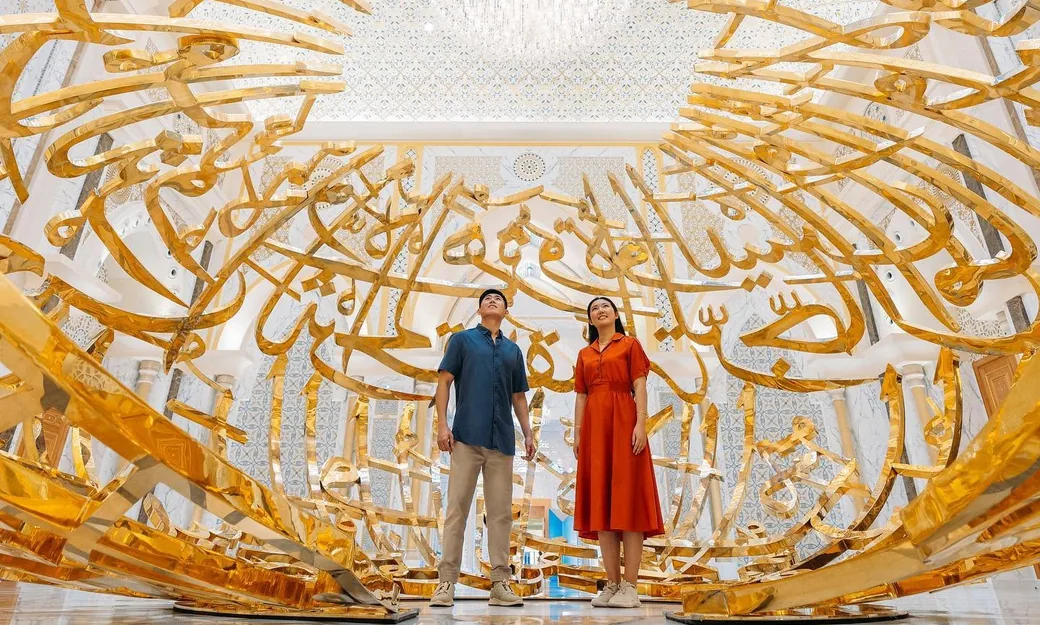 Visitors beneath the monumental Arabic calligraphy installation at Qasr Al Watan