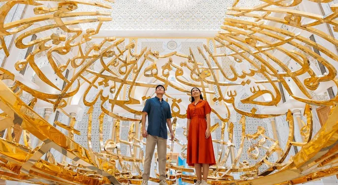 Visitors beneath the monumental Arabic calligraphy installation at Qasr Al Watan