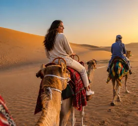 Camel rider following a handler through golden desert dunes