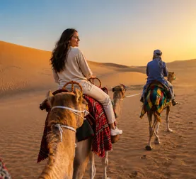 Traveller riding a camel across Abu Dhabi dunes at sunset