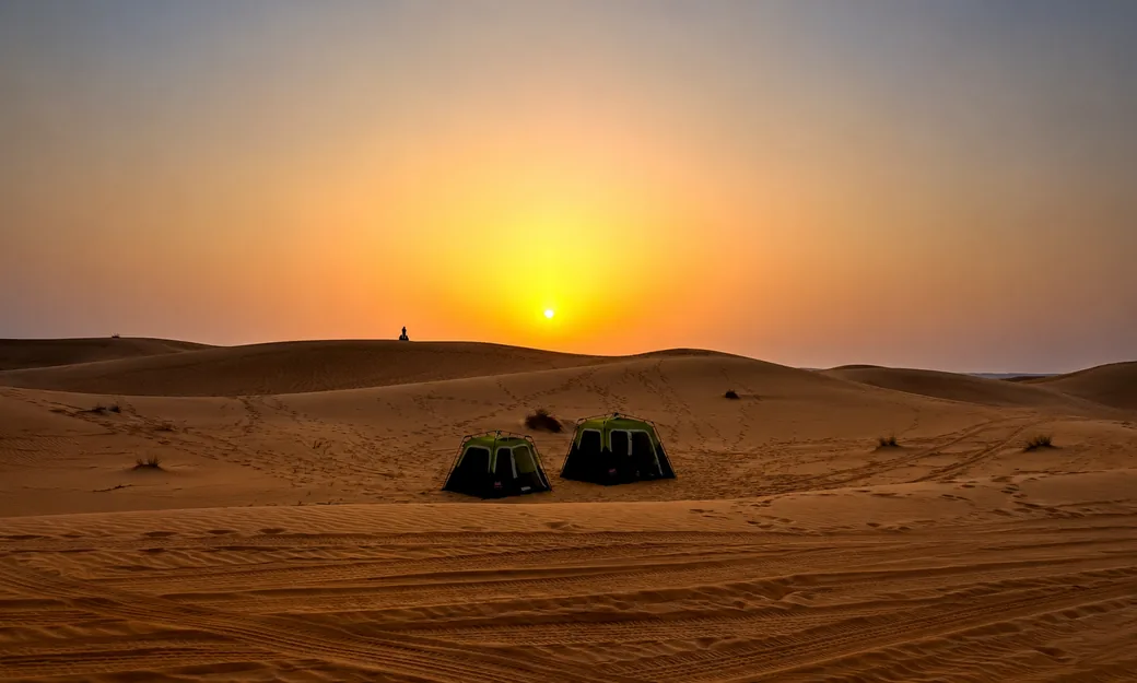 Two private overnight tents beneath an Abu Dhabi desert sunset