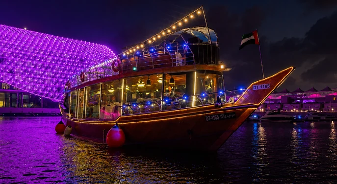 Traditional wooden dhow sailing at Yas Marina beside the illuminated Yas Island waterfront
